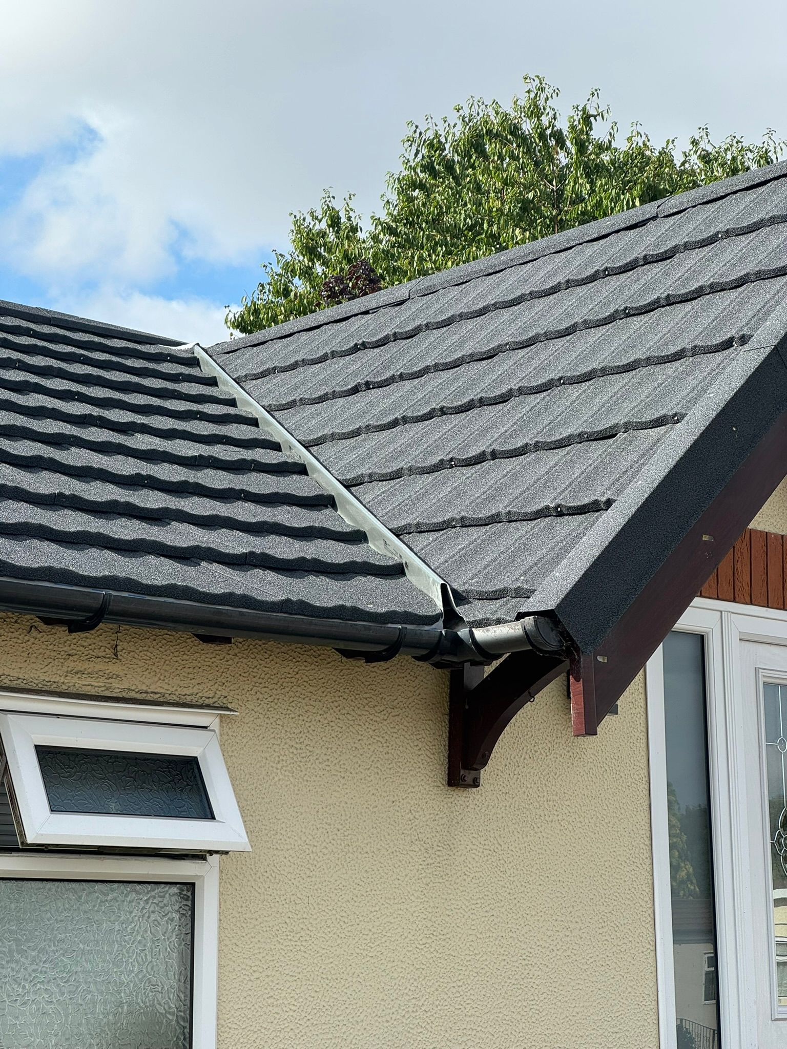 Close-up of a new grey tiled roof with black guttering and downpipe