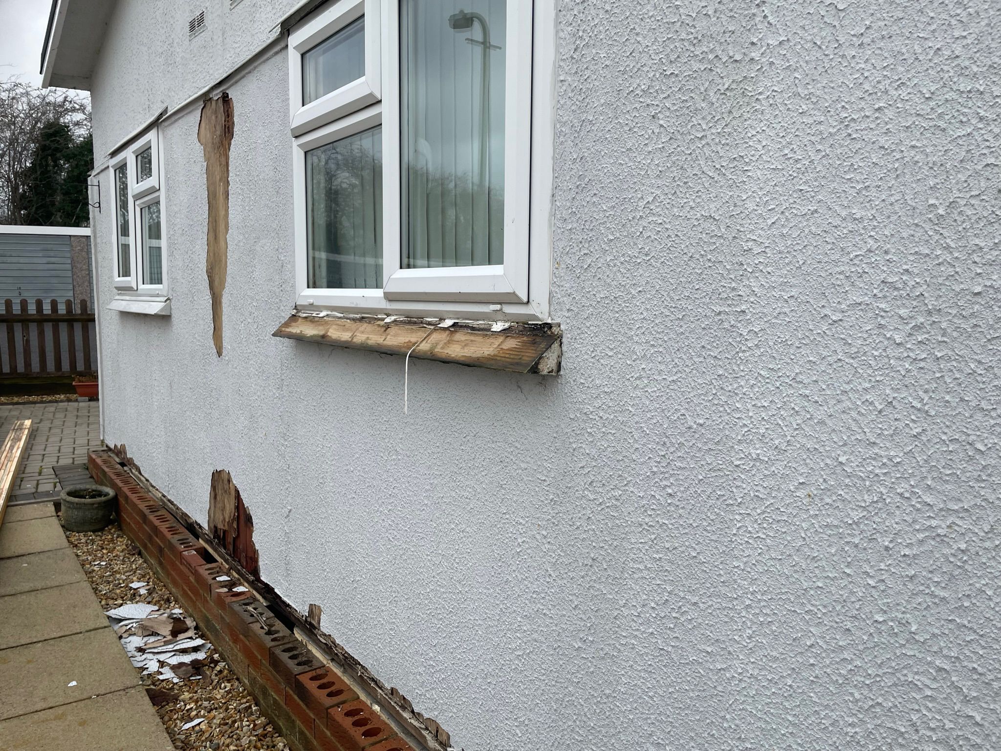 Decayed timber window sill and base rail on an old rendered park home before repair