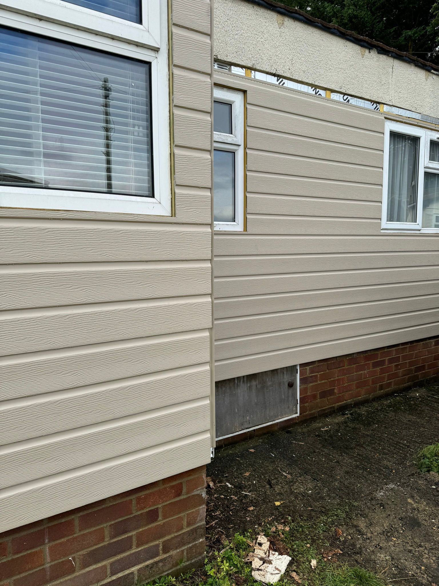 New tan cladding meeting the old render mid-installation